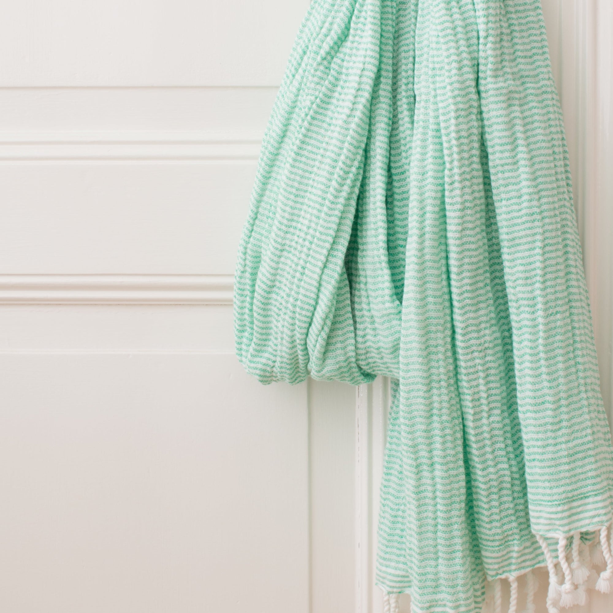 Serviette fouta couleur vert jade pendue à une poignet de porte 
